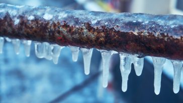 Many small icicles have frozen on a rusty pipe in the street in